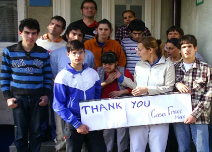 Beneficiari ai programului Locuitul, în fața Casei Franz Max, ținând un afiș de mulțumire